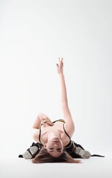 Young woman is kneeling on a white studio background, gracefully arching her back and extending her arm above her head