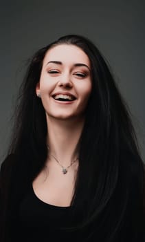 Happy brunette woman in a stylish black shirt smiles joyfully in a studio portrait against a grey background, exuding beauty and a carefree vibe