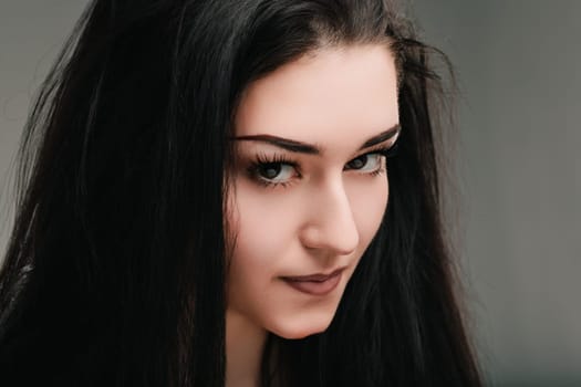 Youthful woman with dark hair is posing in front of a gray background, her expression suggesting deep thought and introspection