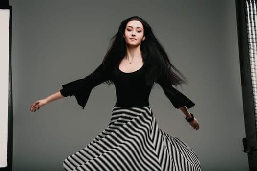 Young woman is spinning gracefully in a studio, her striped skirt flowing around her. She is wearing a black top and has long, dark hair