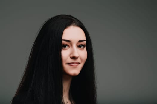 Young woman with long dark hair deep in thought, smiling subtly with a serene expression, contemplating important decisions against a neutral gray backdrop