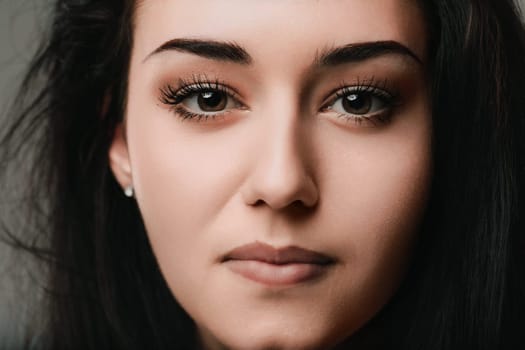 Close up of a young woman with brown eyes and long dark hair, her neutral expression hinting at a moment of quiet reflection