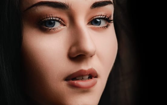 Young woman with dark hair poses against a black backdrop, showcasing her natural beauty. Her flawless skin and expressive eyes radiate freshness and vitality, exuding glamour and sophistication
