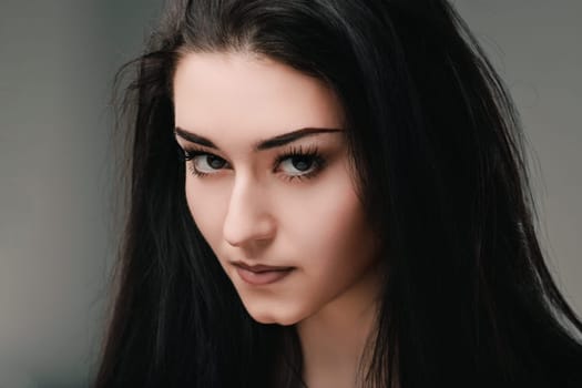 Young woman with long, dark hair poses thoughtfully in a serene studio, exuding depth and glamour