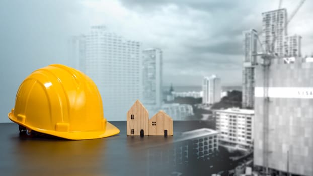 Hard hat and wooden house mockup placed at black tabletop on double exposure background of high building and construction site. Project planning presentation, project presentation and project design.