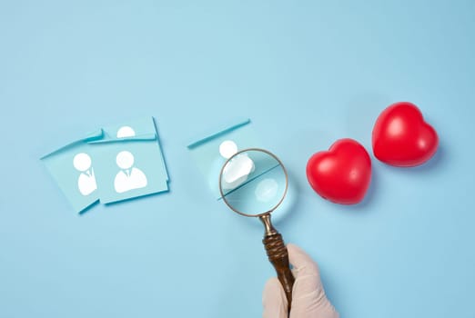 Female hand holding magnifying glass and red hearts on blue background, donor selection