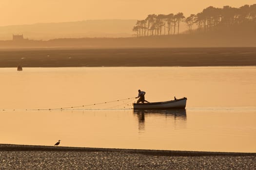 A fisherman hauling in his nets at sunset on the coast near Caernarfon in Gwynedd in Wales.