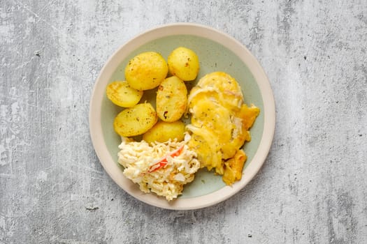 Overhead view of baked pork fillet with melted cheese and onion served with fried potato and cabbage salad