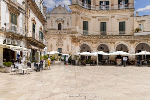 Martina Franca, Italy, Apulia - May 25, 2024:  Maria Immaculate Square (Piazza Maria Immacolata), historical portici in neoclassical style. Basilica of San Martino in a distance