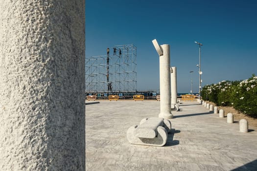 Workers dismantle stage scaffolding after a music event held on the beach near Piazza Primo Maggio in Pescara, Italy. Columns and stone benches grace the seafront of the Abruzzo city.