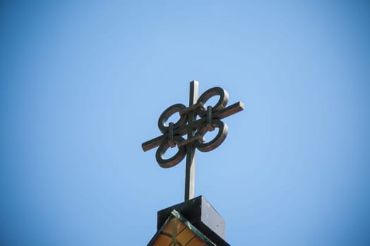 A unique metal cross on a top of building, featuring four interconnected circles at its center against a clear sky.