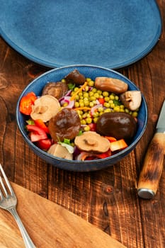 Dietary vegetable salad with marinated pickled mushrooms, green peas in bowl.