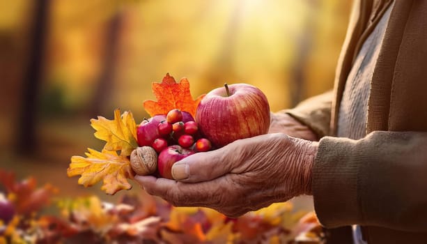 Closeup old man hands holding apple, nuts and berries with colorful leaves over autumn garden background. Farmer picks up the harvest, fall seasonal concept