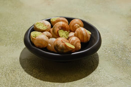 Edible snails Escargot stuffed with spicy herbal butter on green background