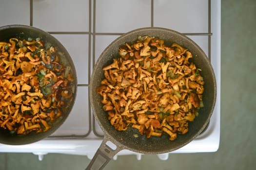 Overhead view of frying chanterelle mushrooms in two frying pans on gas stove in the kitchen