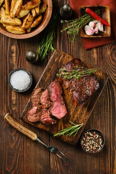 Overhead view of juicy grilled top blade beef steak on wooden cutting board with garnish