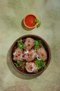 Vertical composition with fried beef or lamb patties wrapped in fat gut and small bowl with adjika sauce