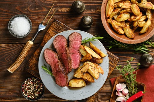 Overhead view of sliced beef steak with baked potato wedges and scented herbs on a plate