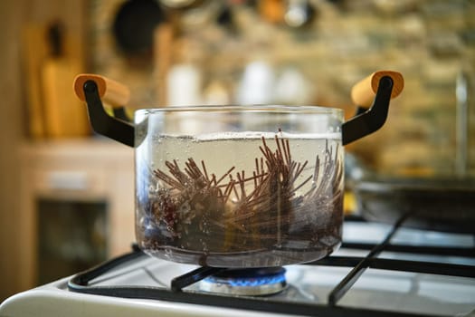 Close-up view of boiling black rice noodles in transparent glass saucepan on a gas stove