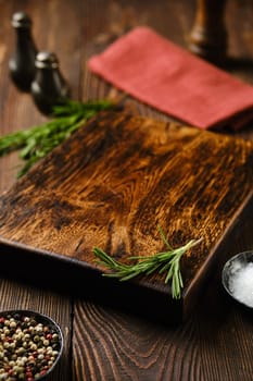 Empty wooden chopping board on kitchen table with spice and herbs