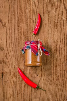 Overhead view of spicy jar with chilli pepper sauce or adjika on wooden background