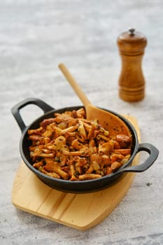 Fried chanterelles in cast iron skillet on wooden serving board