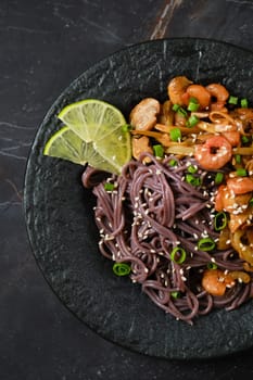 Close-up view of a plate with spicy black rice noodles, shrimps and mushrooms on black background