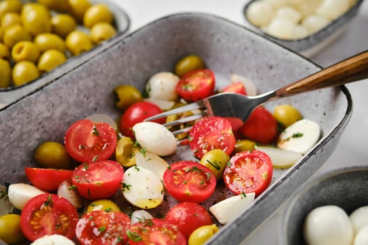 Eating mozzarella, tomato and olives salad seasoned with olive oil and balsamic vinegar