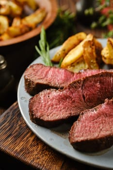 Close-up view of sliced roasted beef steak with baked potato wedges and scented herbs on a plate