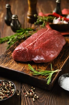 Raw beef top round steak on wooden cutting board surrounded with spice and herbs