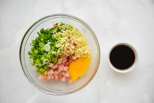 Overhead view of a glass bowl with chopped shrimps, spring onion, ginger and egg yolk