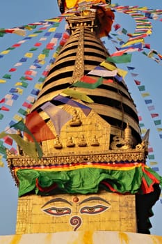 The top of the Swayambhunath Stupa, Temple, many colorful prayer flags are dancing in the wind around a golden face, Kathmandu, Nepal 2022