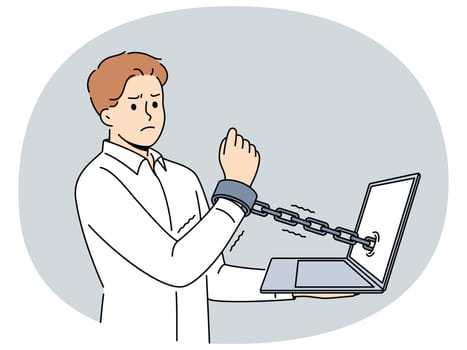 Man handcuffed to laptop symbolizes slavery of clerks and freelancers working through internet. Guy suffers from online addiction and slavery or lack of time for rest associated with strict deadlines