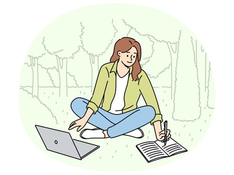 Woman student is sitting on lawn making notes in notebook and using laptop enjoying working in park. Happy girl student watching educational video and writing notes located in park