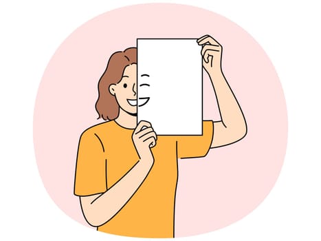 Smiling woman holding piece of paper with emoji in front of face and looking at screen. Positive girl with partially painted smile is sharing good mood and positive emotions with you.