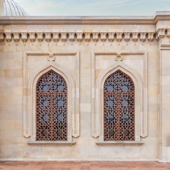 Intricate wooden windows adorn a beautifully crafted stone facade, showcasing traditional architectural style at the courtyard of Bibi-Heybat Mosque, Baku, Azerbaijan