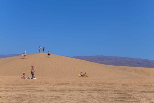 Maspalomas, Gran Canaria: March 20, 2025: Group of tourist people sunbathing at the Natural Reserve of Dunes of Maspalomas, golden sand dunes. Canary Islands, Spain