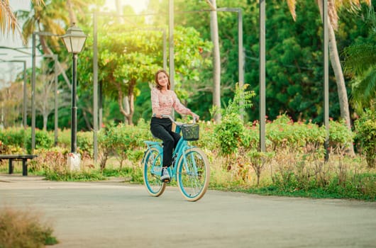 Happy girl riding a bicycle in a park at sunset. Portrait of smiling young woman riding a bicycle in a nice park
