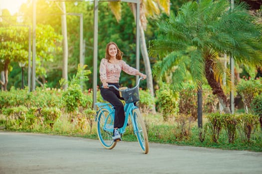 Cheerful Latin girl riding a bicycle in a green park. Beautiful and smiling young woman riding a bicycle in a nice park, looking at camera