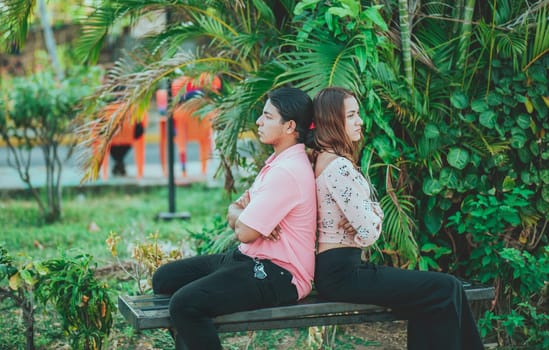 Upset young couple sitting back to back on a bench. Unhappy couple arguing on a public bench. Concept of couple problems and crisis