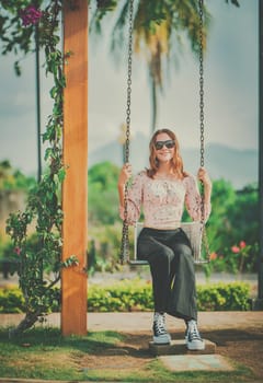 Portrait of a smiling girl sitting on a swing in a nature park. Happy young woman sitting on a swing in a nature park