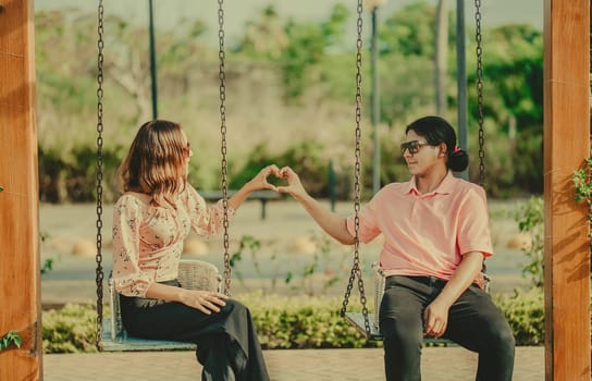 Young couple in love sitting on a swing making a heart shape. Happy couple in love on a park swing making a heart shape