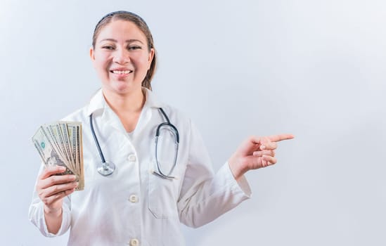 Happy female doctor holding money and pointing to side. Beautiful female doctor showing money and pointing side