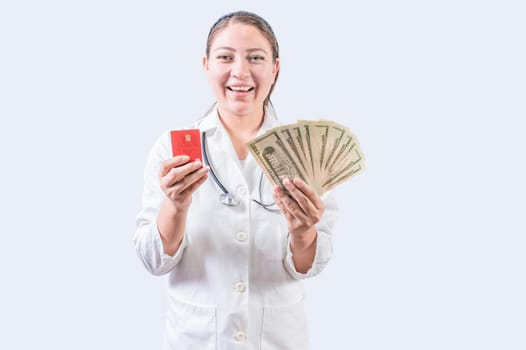 Happy female doctor holding credit card and money isolated. Smiling young female doctor holding money and credit cards
