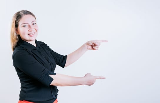 Happy latin woman pointing a promo isolated. Cheerful girl pointing an offer isolated. Beautiful young girl pointing to a banner to the side