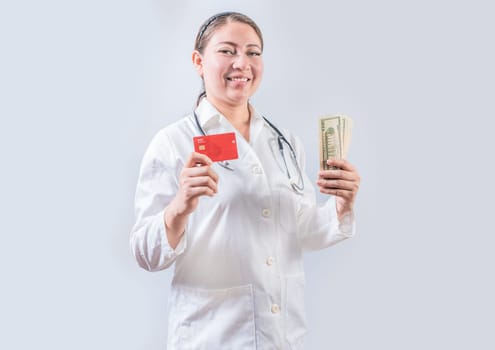 Beautiful and smiling female doctor holding money and credit cards. Happy female doctor holding credit card and money isolated