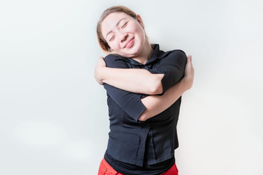 Serene girl hugging herself isolated. Positive woman hugging herself with sincere smile with grateful gesture