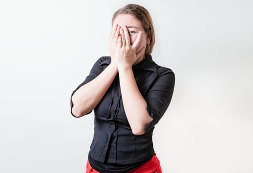 Embarrassed girl covering her face and looking at the camera. Shy girl covering her face and looking at the camera isolated