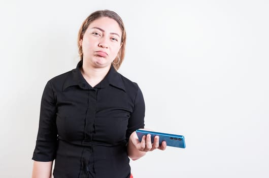 Young skeptical woman with cell phone isolated. Indifferent girl holding cell phone isolated. Sad woman with cell phone looking at camera
