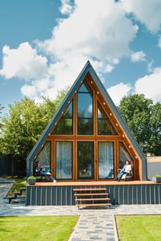 Mother and daughter sitting on a folding chairs on the terrace of a tiny triangular house